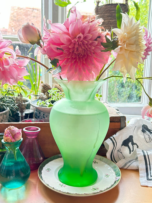 Photo of a green handmade glass dahlia vase in front of a cottage window pain