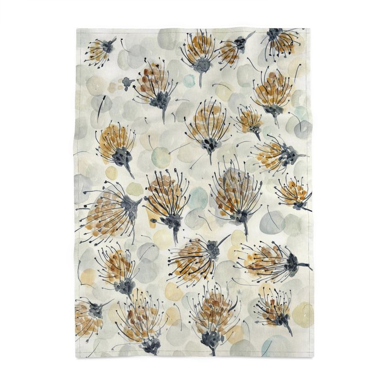 A tea towel with a watercolor-style botanical design featuring pincushion proteas in shades of gold, gray, and black, along with soft, abstract circular shapes in muted tones. The towel is laid on a white background.